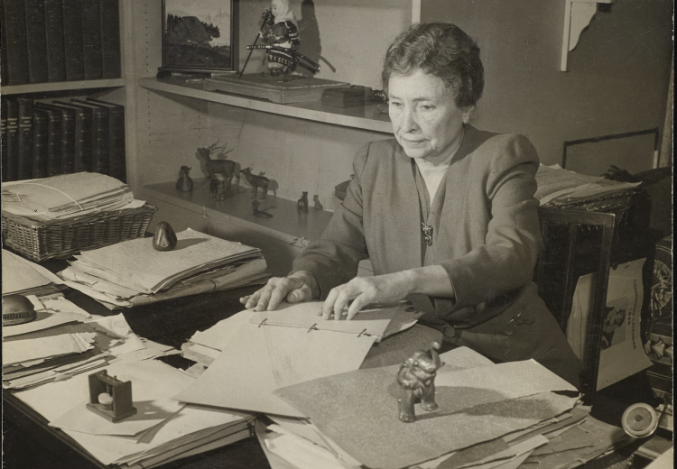 Photograph of Helen Keller seated at her desk and reading text in braille in Westport, Connecticut in 1950.